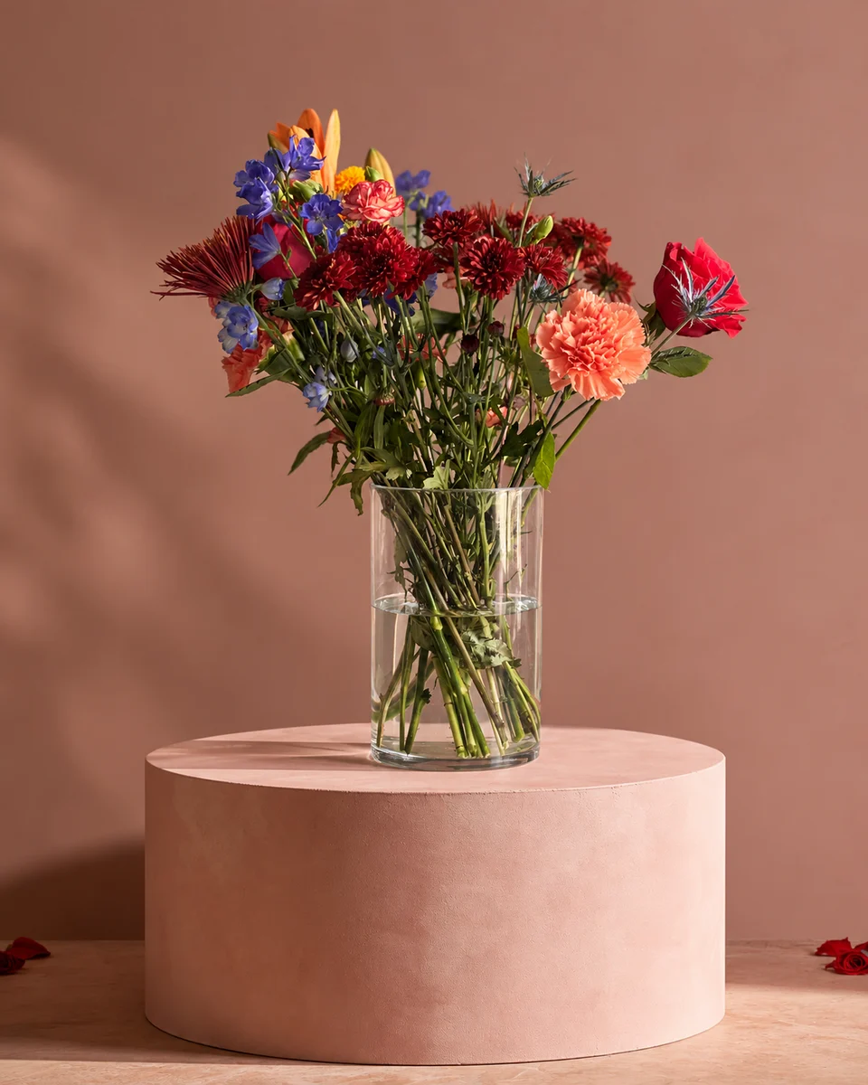 Illustrative test example: Mixed arrangement in a glass vase on a blush pink pedestal against a dusty rose wall
