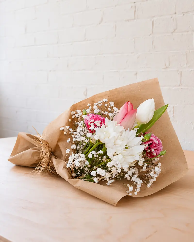 Example with sample flowers: a wrapped bouquet in the Plywood table · white brick room, kept as made